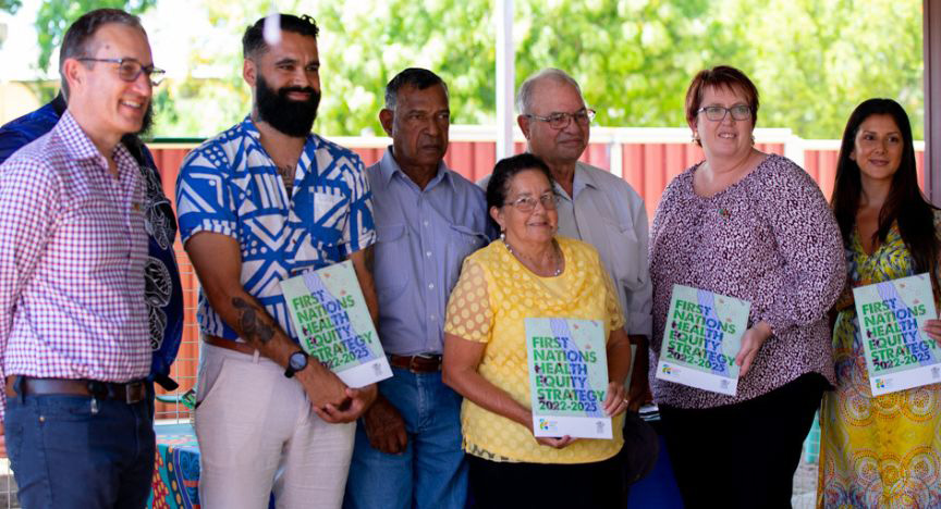 Seven people standing in a line holding copies of the printed Health Equity Strategy.