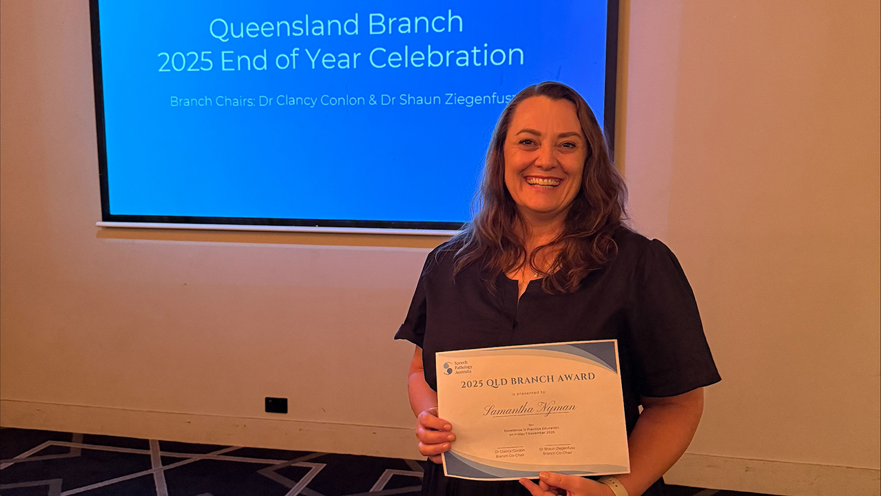 A brunette woman smiles while holding an award certificate in front of a green screen that says Queensland Branch 2025 End of Year Celebration