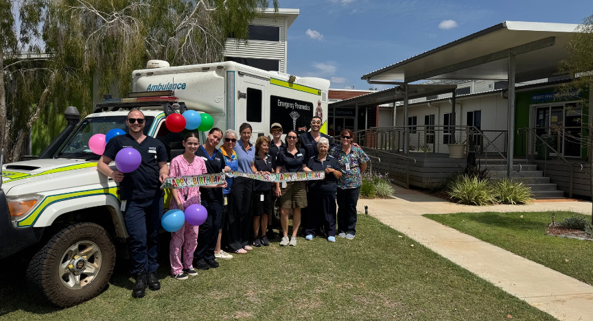 A group of smiling people stand in front of an ambulance.