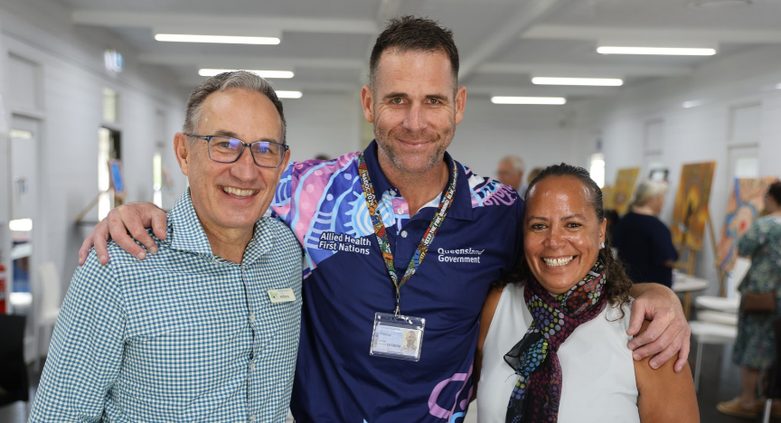 Three people smiling at the camera arm-in-arm in a crowded room.