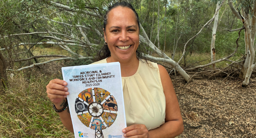 A woman with her dark hair tied back smiles while displaying the front page of a book with a colourful windmill on the cover.